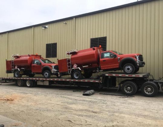 Hauling two red Ford F-550 fuel trucks on a step deck trailer.