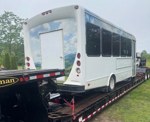 Shuttle bus hauling on a drop deck trailer.