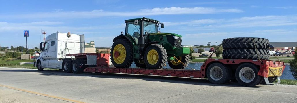 John Deere tractor secured on a lowboy trailer with spare tires